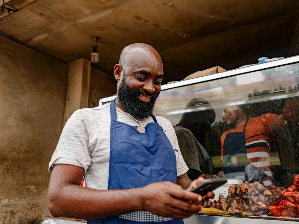 Food stall owner in an apron smiling at an order on his phone